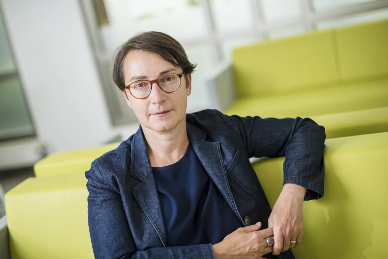 Portrait der DF-Vorsitzenden Dr. Beate von Miquel, die auf einem Sofa sitzt und entschlossen in die Kamera schaut